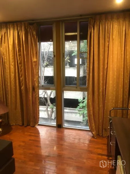Shophouse for rent in Bang Rak, Bangkok - Tall window with gold curtains and city view beside polished wood floor.