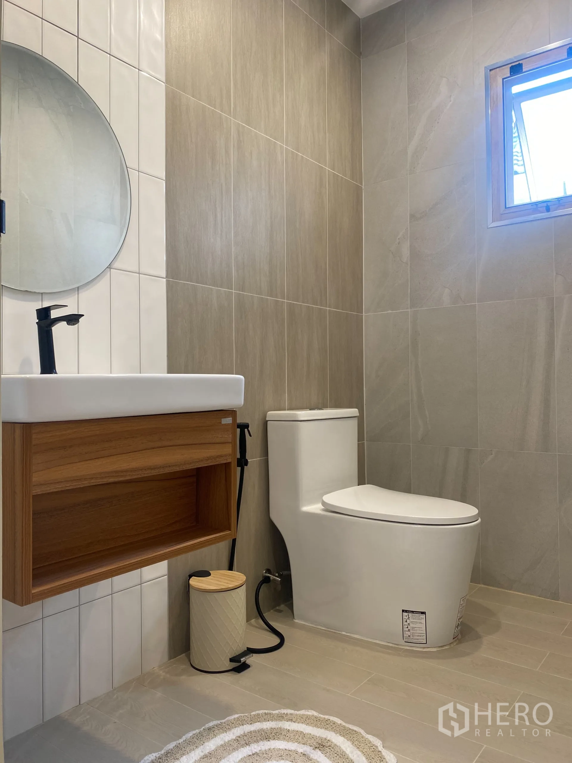 Detached House for sale in Suan Luang, Bangkok - Guest bathroom with round mirror, wood vanity and neutral wall tiles.