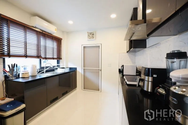 Detached House for rent in Bang Phli, Samut Prakan - Wide kitchen with long counters, window blinds, and a rear door.