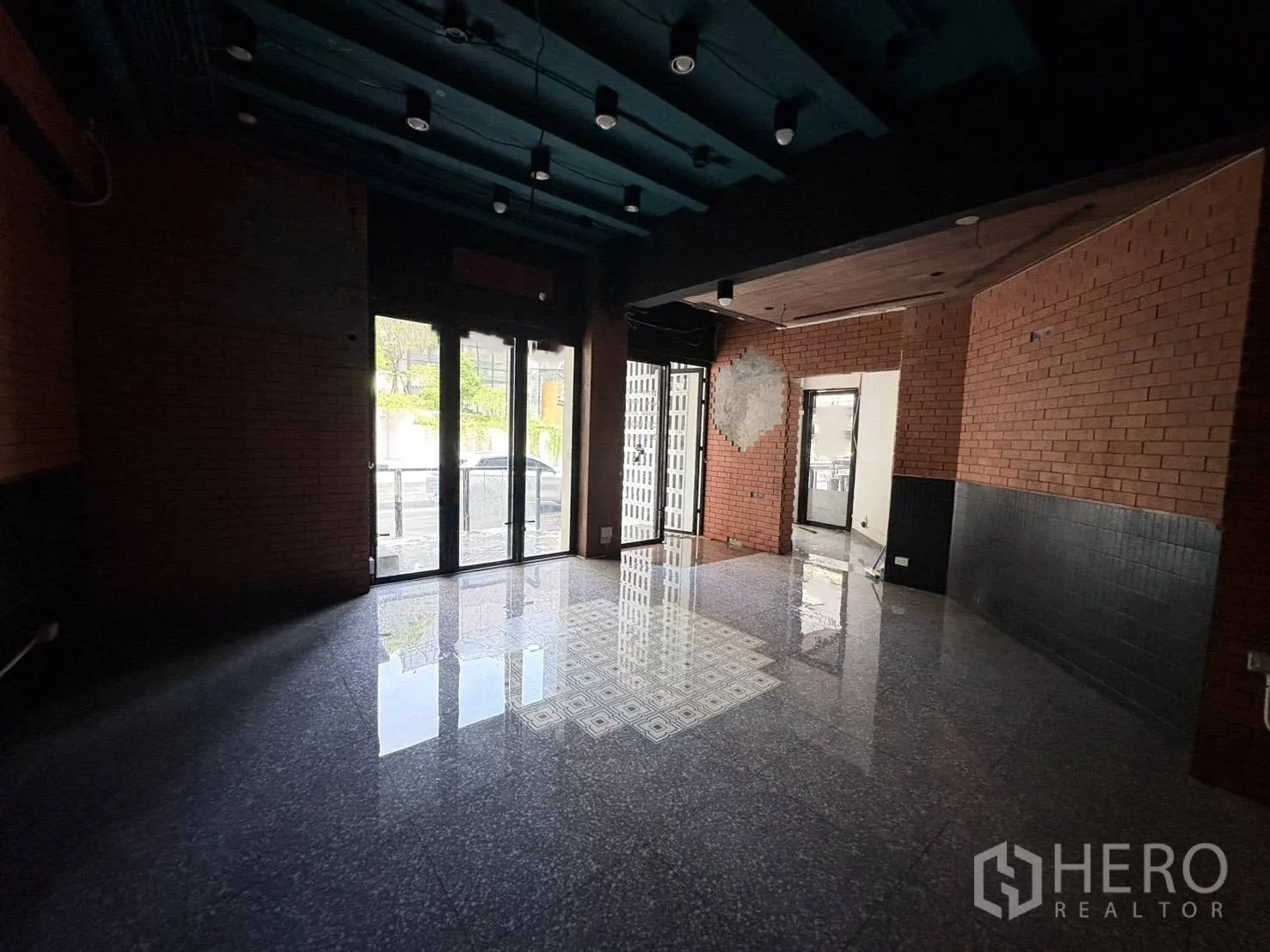 零售空间 for rent in Watthana, Bangkok - 临街零售室内，落地玻璃门、外露红砖墙、抛光石材地面与深色天花射灯。