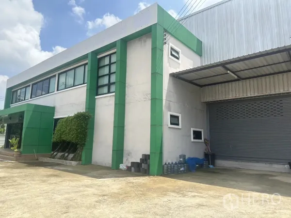 Warehouse for sale in Bang Len, Nakhon Pathom - Side view of the office block with green columns beside a roller shutter entrance.