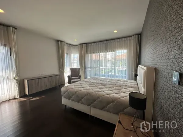 Detached House for rent or sale in Lam Luk Ka, Pathum Thani - Corner master bedroom with large windows, sheer curtains, feature wall, bed and armchair.