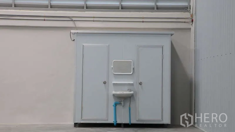 Warehouse for rent in Sam Phran, Nakhon Pathom - Internal restroom module with two doors and a wall‑mounted sink inside the warehouse.