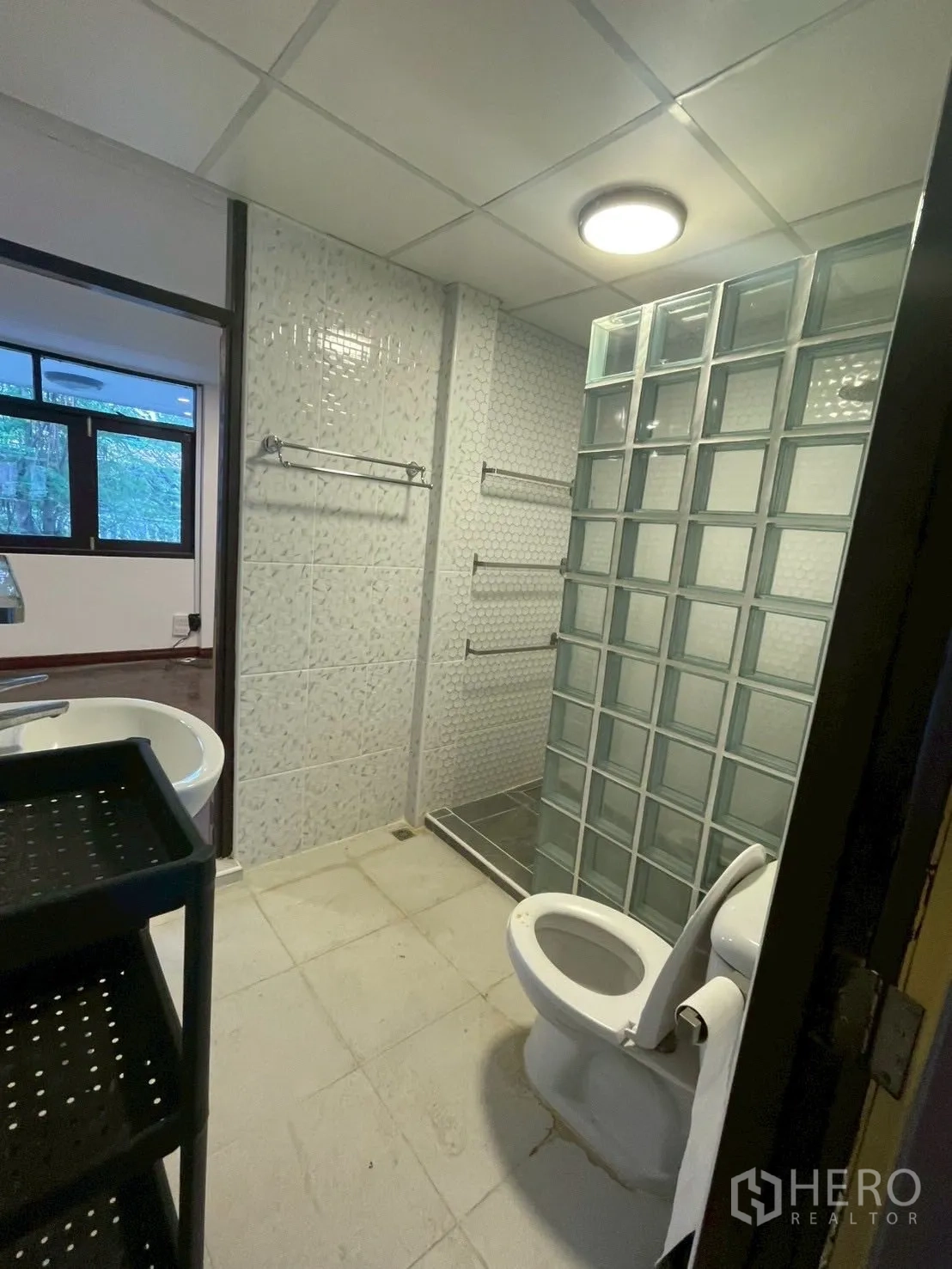 Detached House for rent in Watthana, Bangkok - Bathroom with glass-block shower partition, white tiles, toilet and a vanity basin.