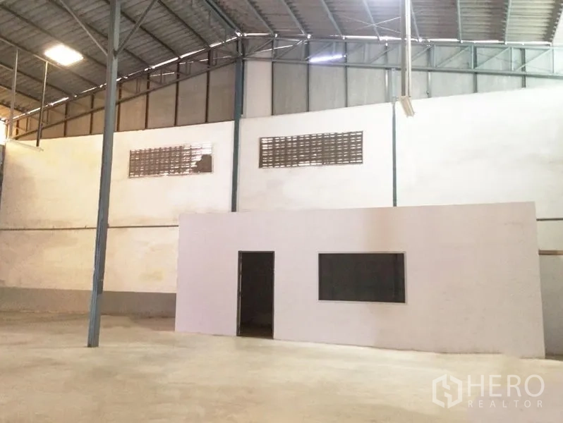 Warehouse for rent in Prawet, Bangkok - Warehouse interior featuring a built-in office room, metal roof structure, and polished concrete surface.