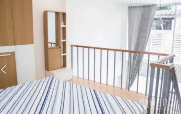Townhouse for rent in Khlong Toei, Bangkok - Loft bedroom with striped bedding, wardrobe, and abundant light from large sliding glass doors.