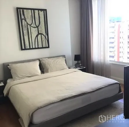 Condominium for rent in Pathum Wan, Bangkok - Master bedroom with king bed, wall art and a city‑view window with long drapes.