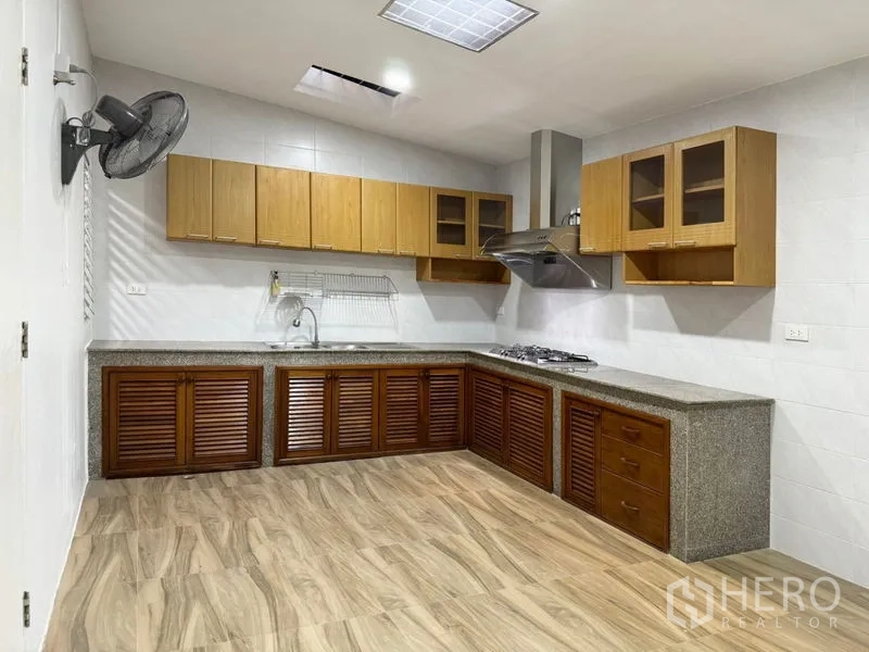 Townhouse for rent or sale in Suan Luang, Bangkok - Family kitchen with L-shaped counters, gas hob, hood and wood cabinets