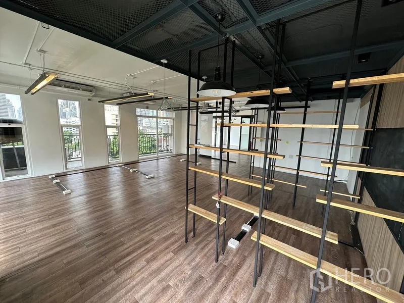 Office Space for rent in Watthana, Bangkok - Open-plan office with a metal-and-wood shelving divider, multiple tall windows with railings, and urban views.
