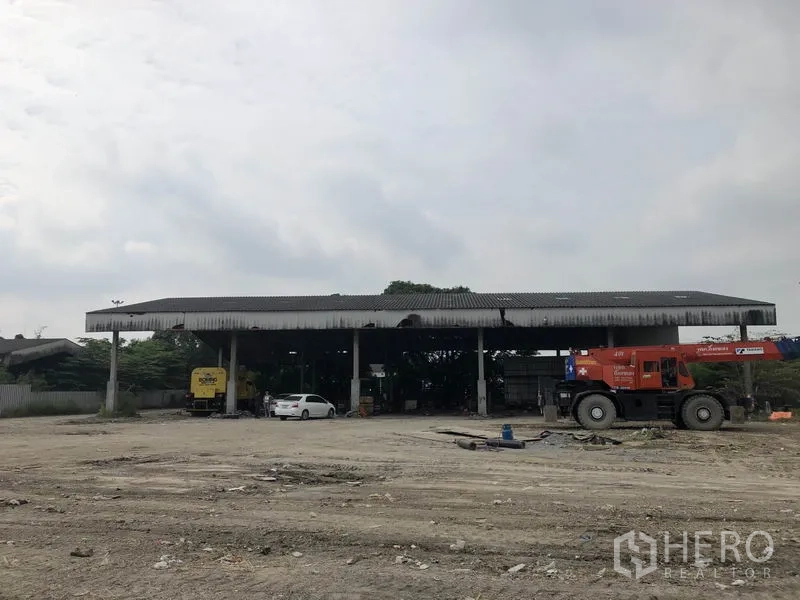 Factory for rent in Phra Nakhon Si Ayutthaya - Wide open-sided metal-roof shed with heavy equipment and cars facing a large yard.