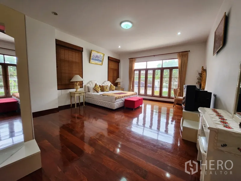 Detached House for rent in Prawet, Bangkok - Sunlit bedroom with large windows and balcony doors over gleaming hardwood floors.