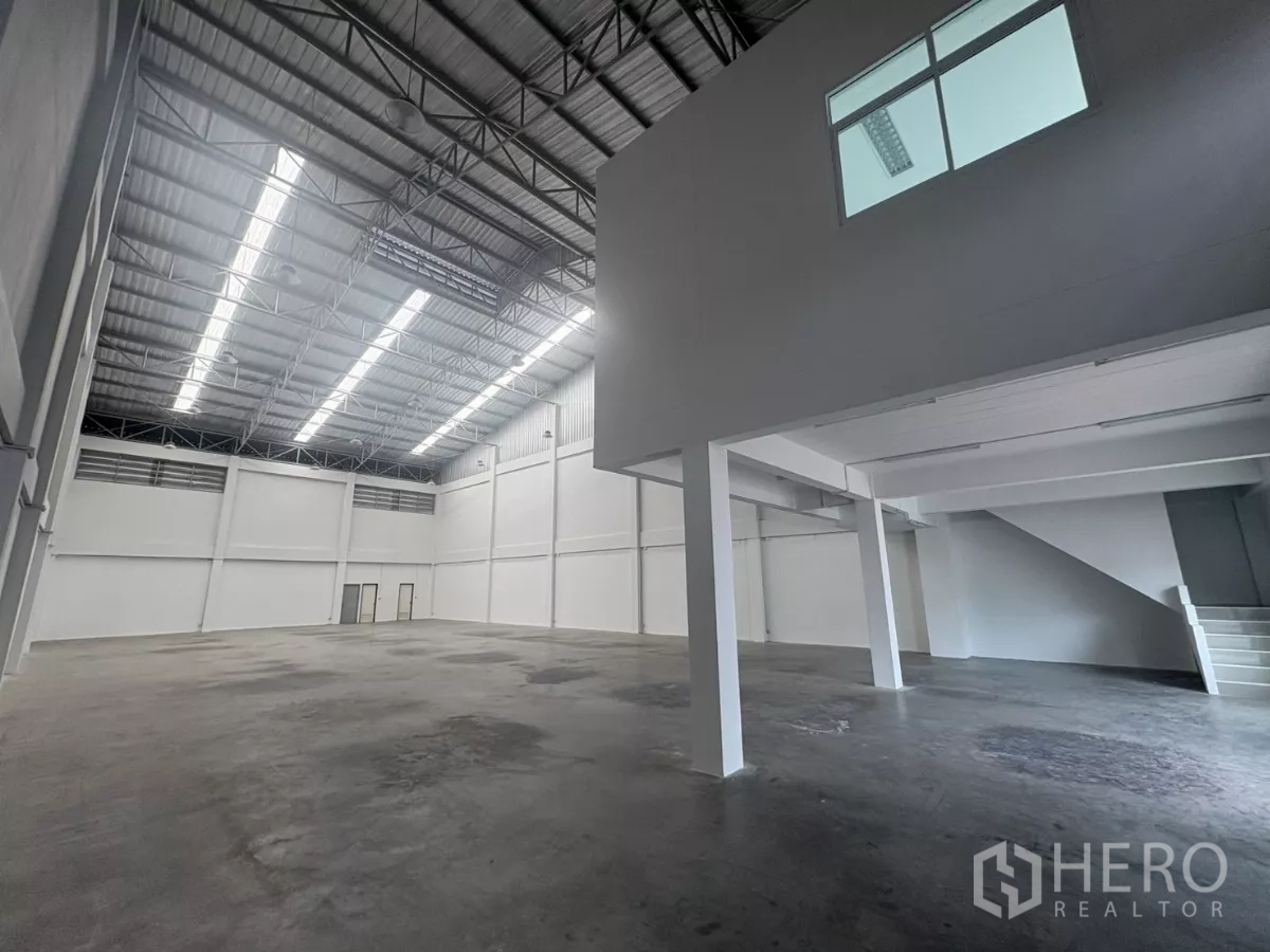 Factory for rent in Phra Samut Chedi, Samut Prakan - Spacious warehouse interior with high steel roof and mezzanine office on the right.
