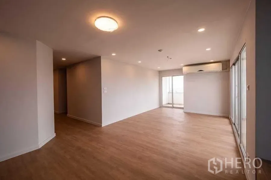 Condominium for sale in Chatuchak, Bangkok - Spacious living room with wood flooring, recessed lights, wall-mounted AC and sliding doors to a balcony.