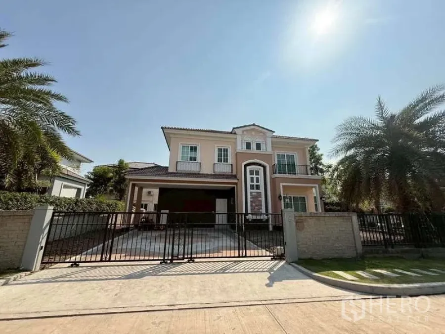 Detached House for sale in Bang Khen, Bangkok - Two-storey detached house with gated driveway and palm trees at the front under a clear Bangkok sky.