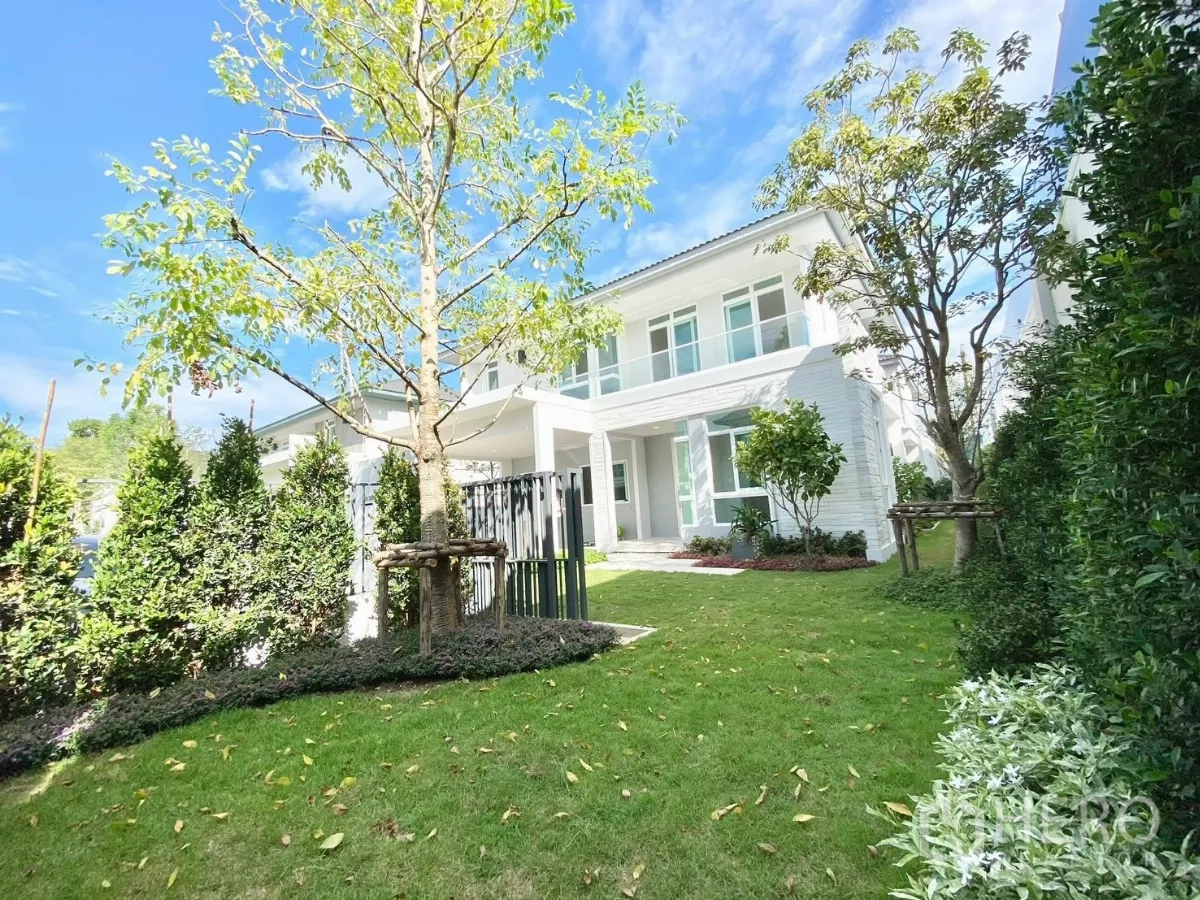 Detached House for rent or sale in Prawet, Bangkok - Modern two-storey white detached house facade with lush front lawn and blue sky.