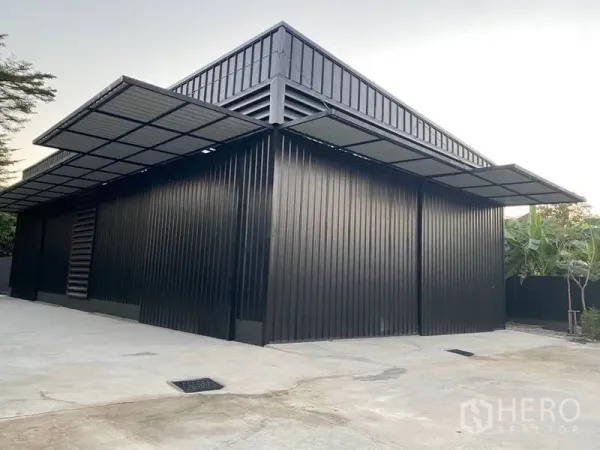 Warehouse for rent in Wang Thonglang, Bangkok - Modern black metal-clad warehouse exterior with large canopy over loading area and concrete yard.