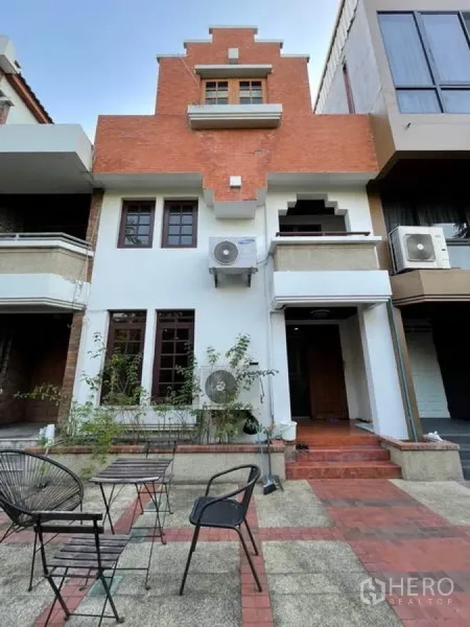 Townhouse for rent in Khlong Toei, Bangkok - Three-storey townhouse facade with red brick and white stucco, balcony and front steps.