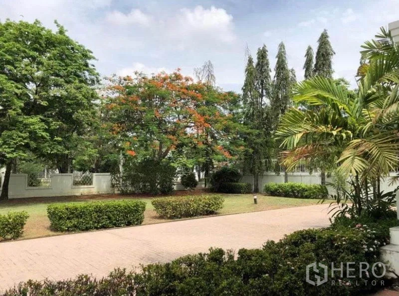 Detached House for sale in Mueang Samut Prakan, Samut Prakan - Tree-lined driveway and landscaped garden with hedges inside a walled compound.