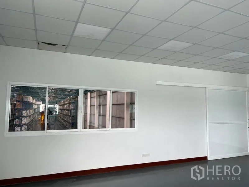 货栈 出租在Lat Krabang, Bangkok - 办公室观景窗，可看到仓库内的货架通道