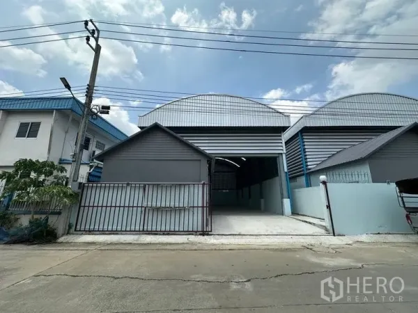 Factory for rent in Pak Kret, Nonthaburi - Front facade showing a tall roller shutter door and concrete driveway leading into the factory.
