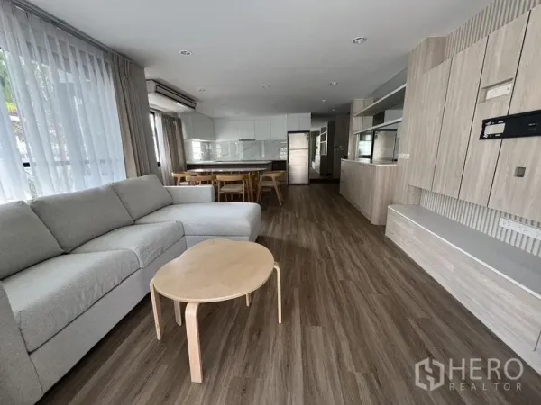 Detached House for rent in Bang Rak, Bangkok - Spacious lounge with full-height windows, wood flooring, and a built-in TV wall facing the seating area.
