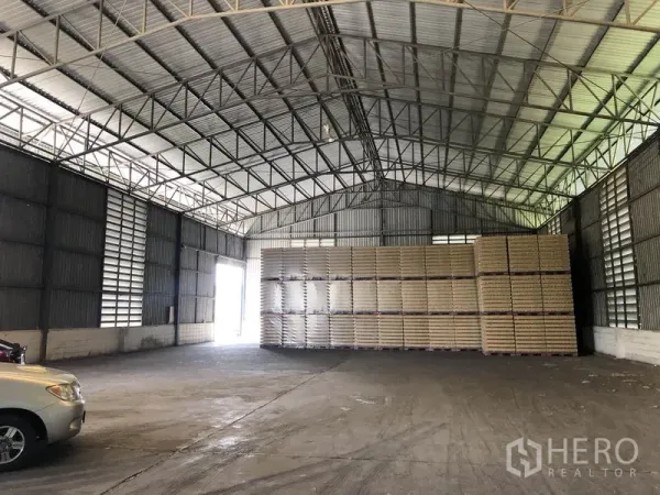 Warehouse for rent in Pathum Thani - Clear-span storage hall with stacked pallets along the wall and a bright side entrance.