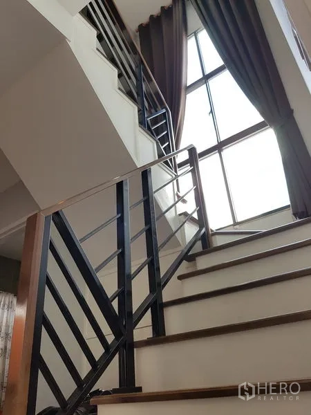 Detached House for sale in Samut Prakan - Staircase with sleek metal railing and a tall window bringing natural light.