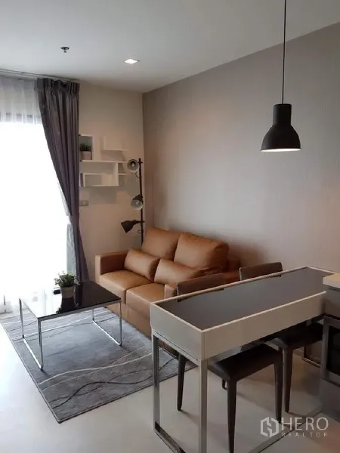 Condominium for rent in Khlong Toei, Bangkok - Cozy living area with tan sofa, black glass coffee table, rug, pendant lighting, and balcony access.