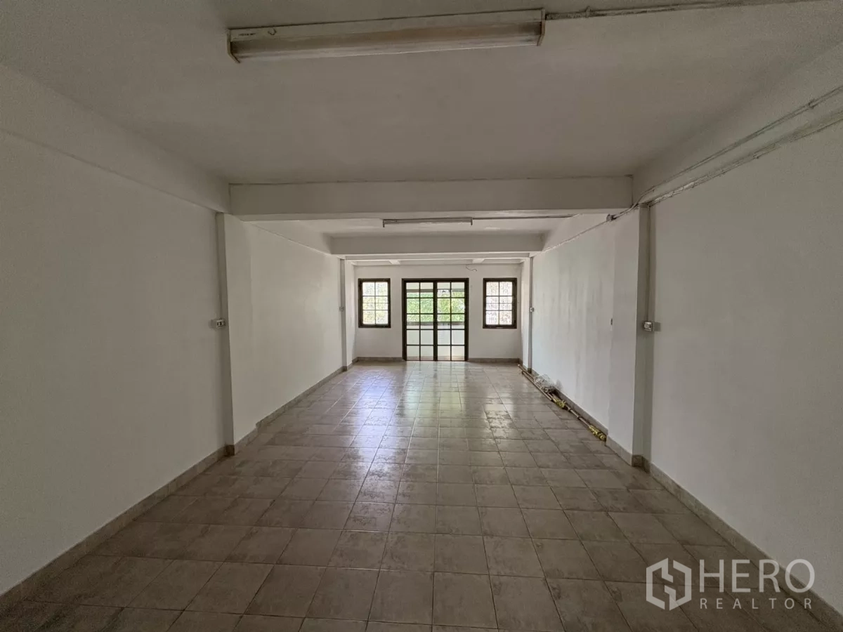 Shophouse for rent in Phra Khanong, Bangkok - Large open‑plan floor with ceramic tiles, white walls and windows at the far end.