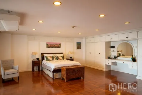 Condominium for rent in Khlong Toei, Bangkok - Expansive master bedroom with recessed lighting, built‑in white wardrobes, dressing vanity and wood floors.