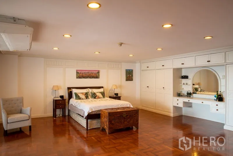 Condominium for rent in Khlong Toei, Bangkok - Expansive master bedroom with recessed lighting, built‑in white wardrobes, dressing vanity and wood floors.