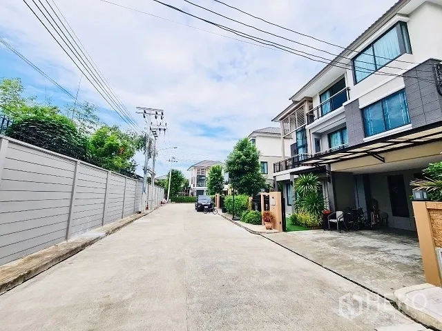 Detached House for sale in Suan Luang, Bangkok - Wide internal road lined with contemporary houses, utility poles, and landscaped plants.