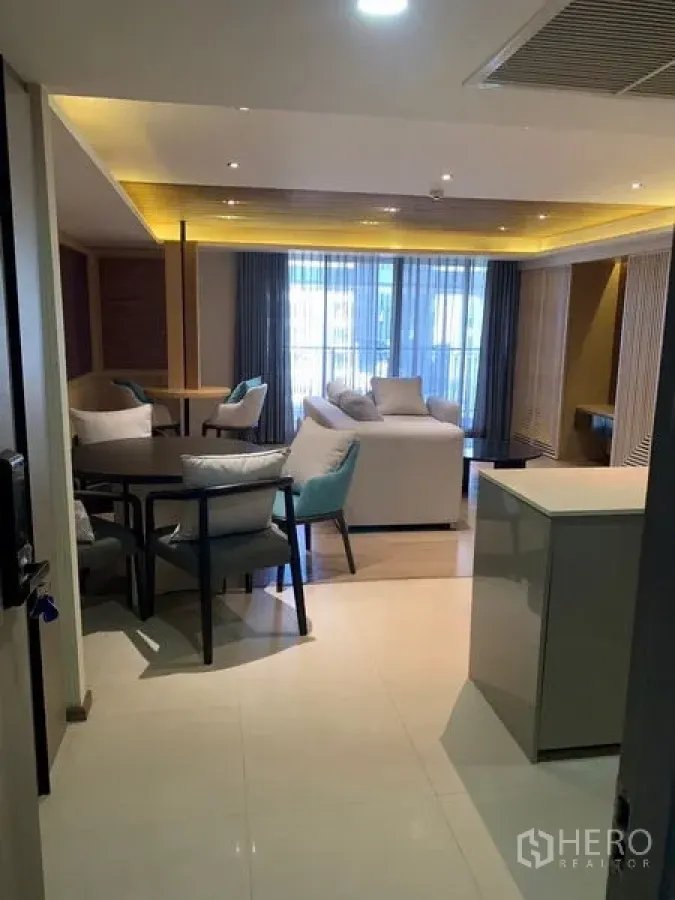 Condominium for rent in Pathum Wan, Bangkok - Open‑plan living room with dining table, sofa seating, and warm ceiling lighting seen from the doorway.