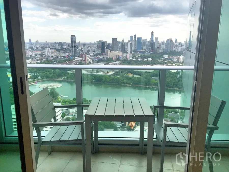 Condominium for rent in Khlong Toei, Bangkok - High-floor balcony with table and chairs overlooking Benjakitti Park lake and the Bangkok skyline.