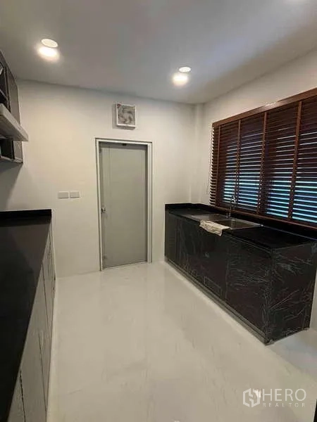 Detached House for rent in Mueang Nonthaburi, Nonthaburi - Closed kitchen with black stone countertops, window blinds and ample cabinets.