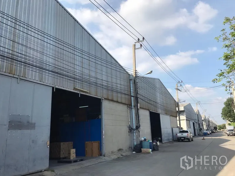 Warehouse for rent in Bang Phli, Samut Prakan - Row of adjoining warehouses along an internal road with power lines and open loading bays.