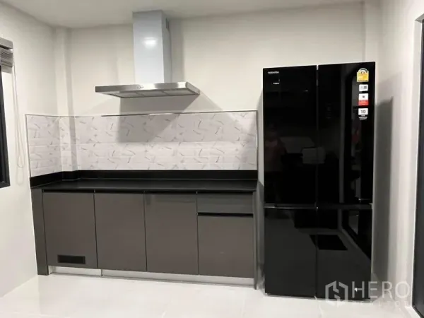 Detached House for rent - Sleek kitchen with extractor hood, glossy cabinets and a black double-door refrigerator.