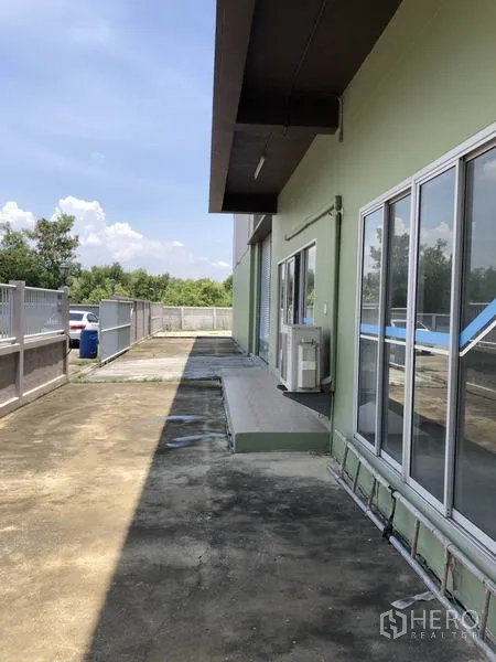 Factory for rent in Pathum Thani - Side walkway with sliding glass doors, air-conditioning unit and driveway.