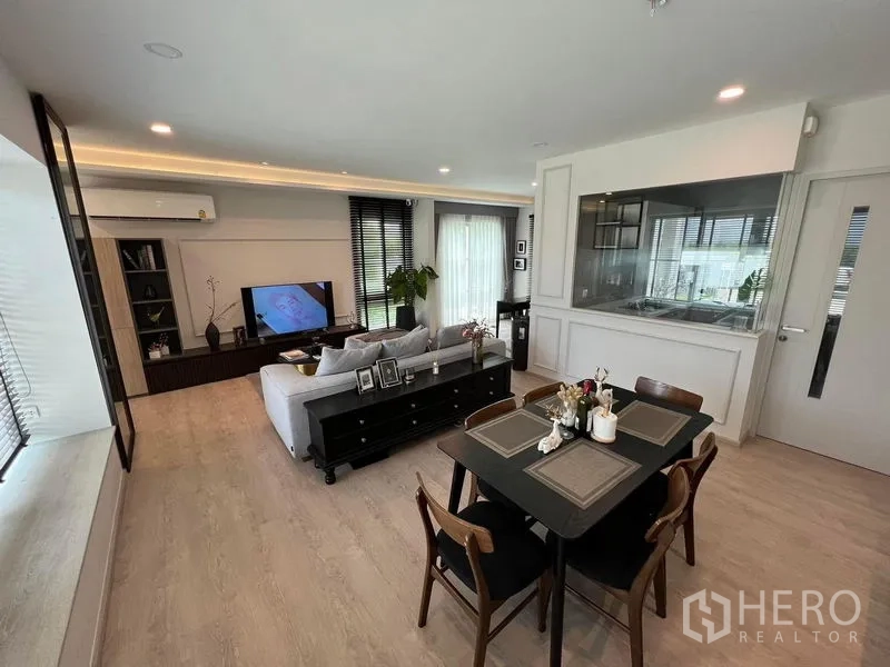 Detached House for rent or sale in Prawet, Bangkok - Living and dining room facing a glass-partitioned kitchen and sliding doors.