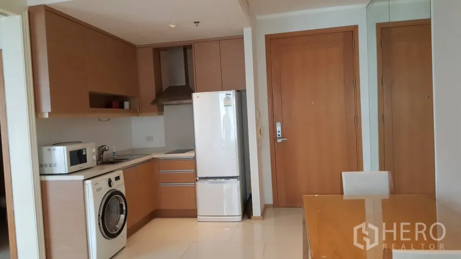 Condominium for rent in Khlong Toei, Bangkok - Modern kitchenette with wood cabinets, washing machine, microwave, fridge and a compact dining area in a Bangkok condo.