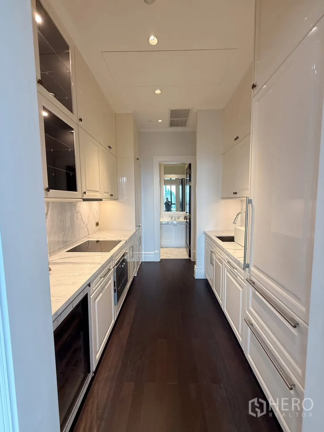 Condominium for rent or sale in Pathum Wan, Bangkok - Long galley kitchen with white cabinetry, marble countertops, and built-in appliances.