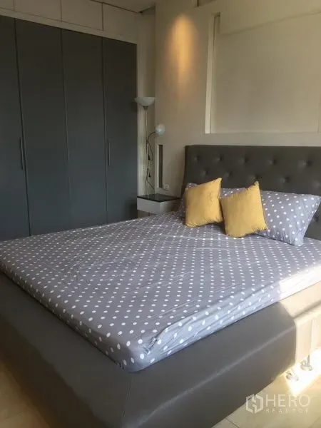 Condominium for rent in Khlong Toei, Bangkok - Master bedroom featuring an upholstered bed with polka dot bedding, good natural light, and wall-to-wall grey wardrobes.