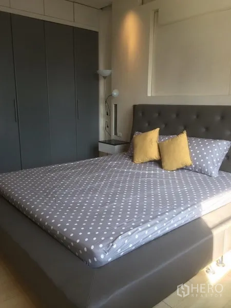 Condominium for rent in Khlong Toei, Bangkok - Master bedroom featuring an upholstered bed with polka dot bedding, good natural light, and wall-to-wall grey wardrobes.