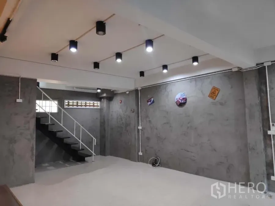 带办公室的家 出租在Khlong Toei, Bangkok - 一层开放式空间，水泥清水墙、顶置射灯与金属楼梯。