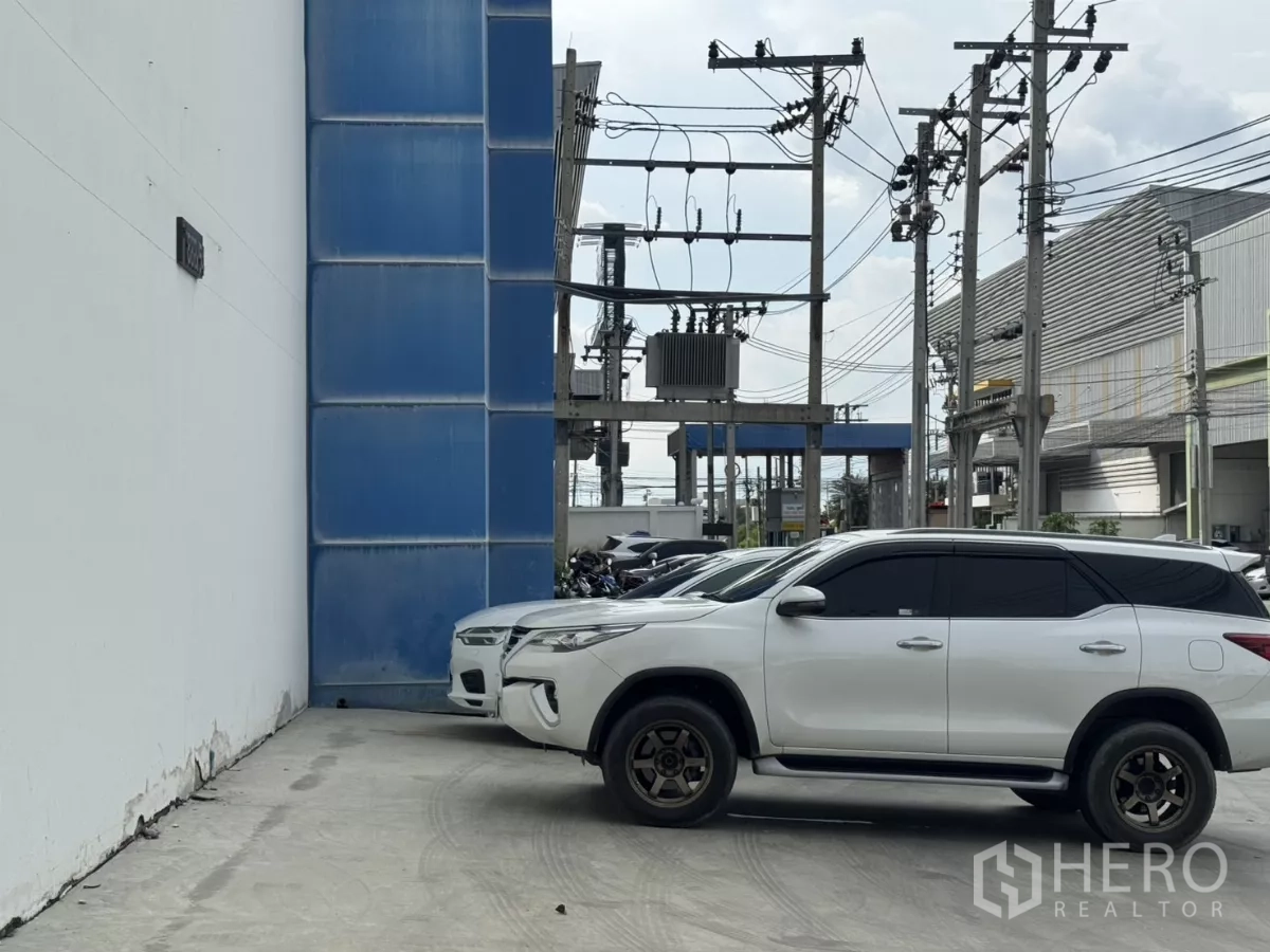 Factory for rent or sale in Bang Phli, Samut Prakan - Front parking area with cars and electrical infrastructure at entry.
