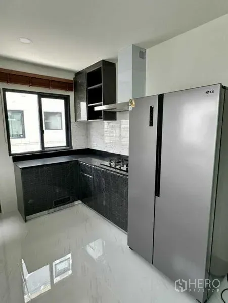 Detached House for rent in Bang Phli, Samut Prakan - Fitted L-shaped kitchen with black cabinets, gas hob, hood, and tall stainless refrigerator.