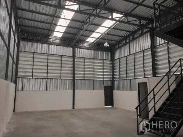 Warehouse for rent or sale in Lam Luk Ka, Pathum Thani - High-ceiling steel-frame warehouse interior with louvered metal walls, skylights and a side access door.