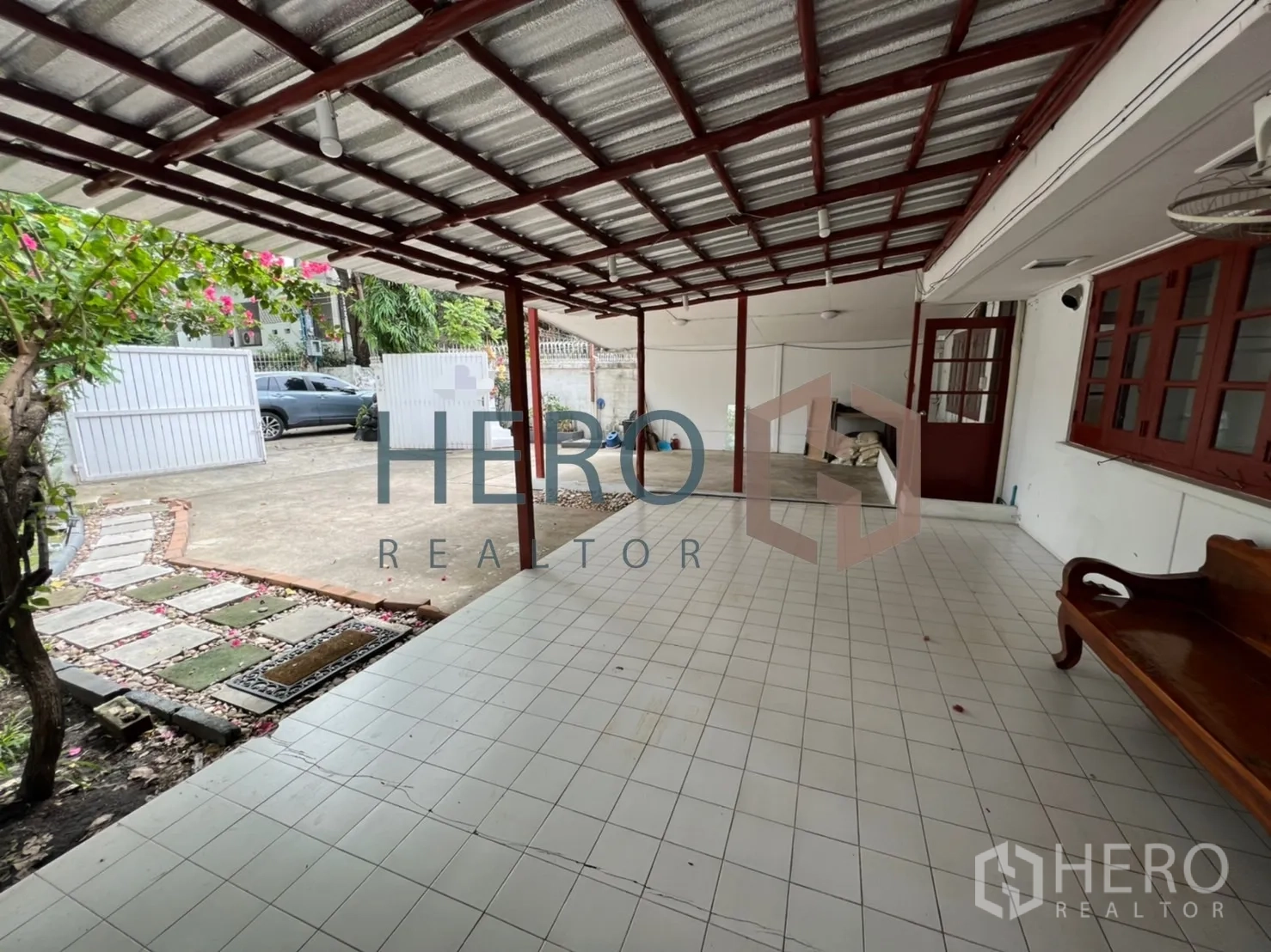 Detached House for rent in Watthana, Bangkok - Covered tiled carport and front veranda with a wooden bench.