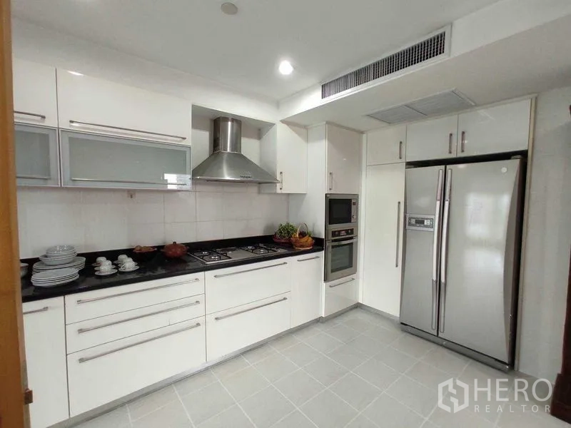 Condominium for rent in Khlong Toei, Bangkok - Modern white kitchen with gas cooktop, range hood, double-door fridge and built-in oven.