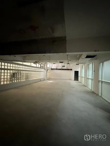 Retail Space for rent - Empty retail space featuring a glass-block side wall, window panels, ducted ceiling and a rear doorway for flexible layout options.